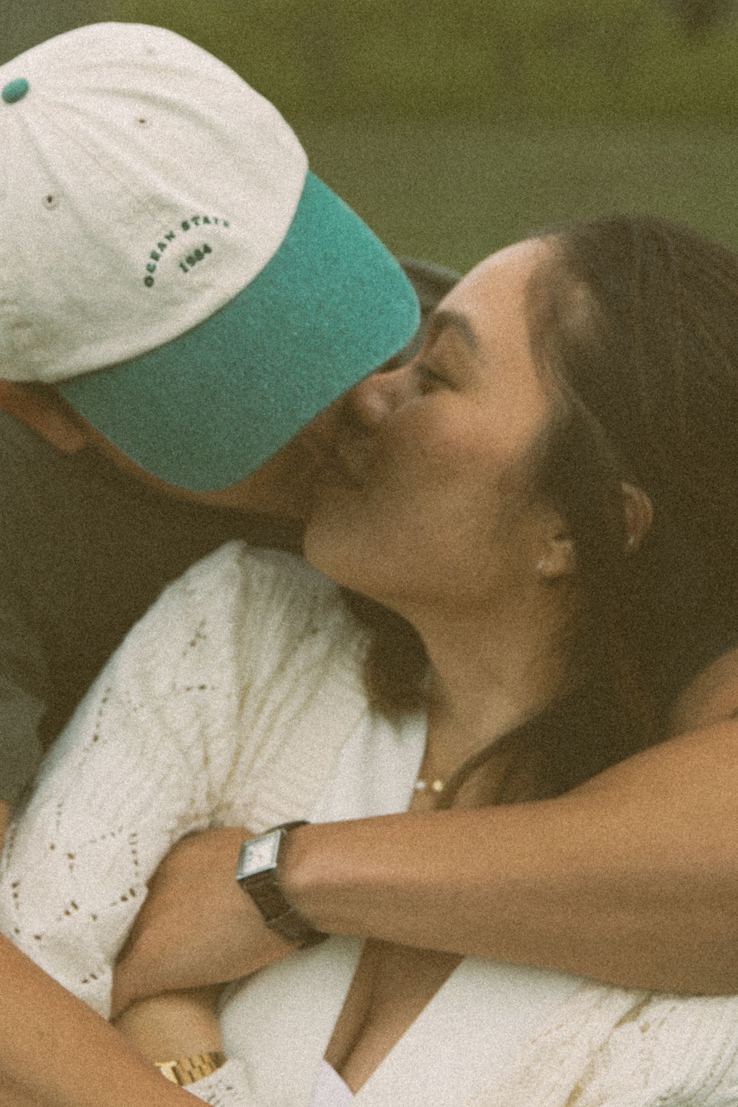 Close-up moment of affection captured outdoors with white baseball cap and natural lighting.