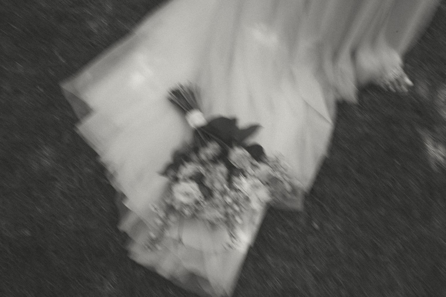 An artistic blur shot of a white wedding dress and bouquet in motion.