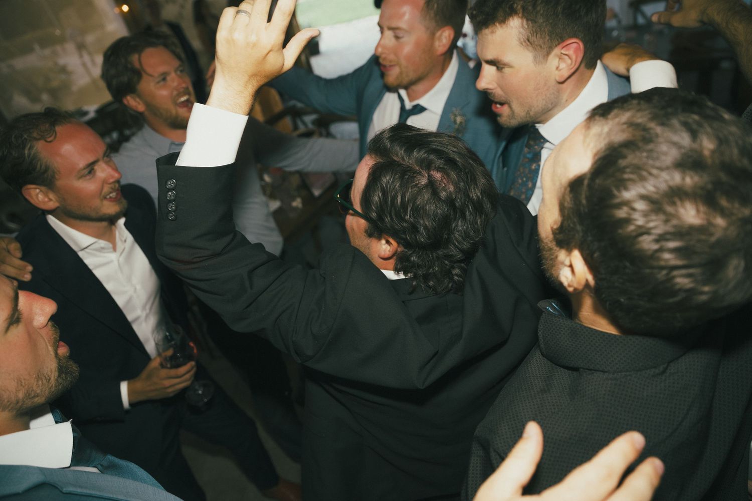 A group of men in formal attire celebrating energetically at what appears to be a reception.