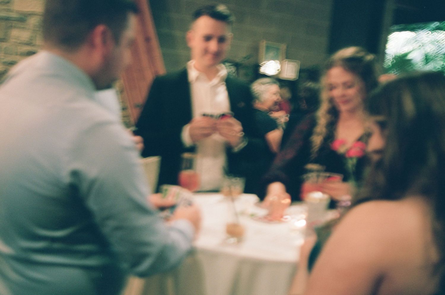 Guests socializing at an elegant indoor event, gathered around a white tablecloth table with drinks.