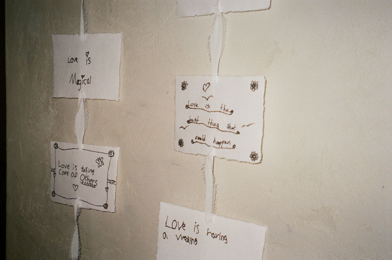 Several handwritten notes posted on a beige wall with white papers and dark writing in an indoor setting.