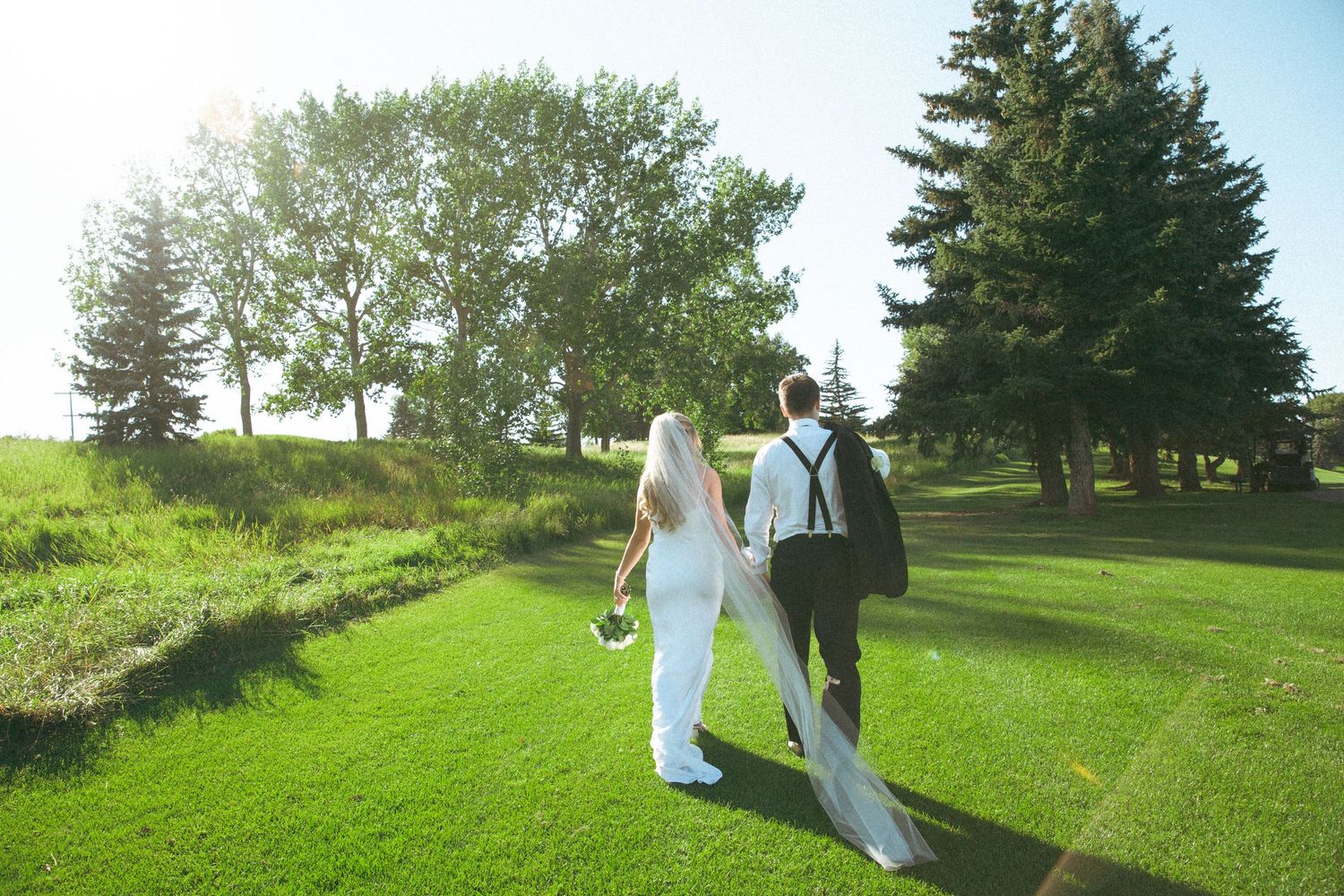 Wedding couple walks on lush green golf course during outdoor ceremony at scenic venue.