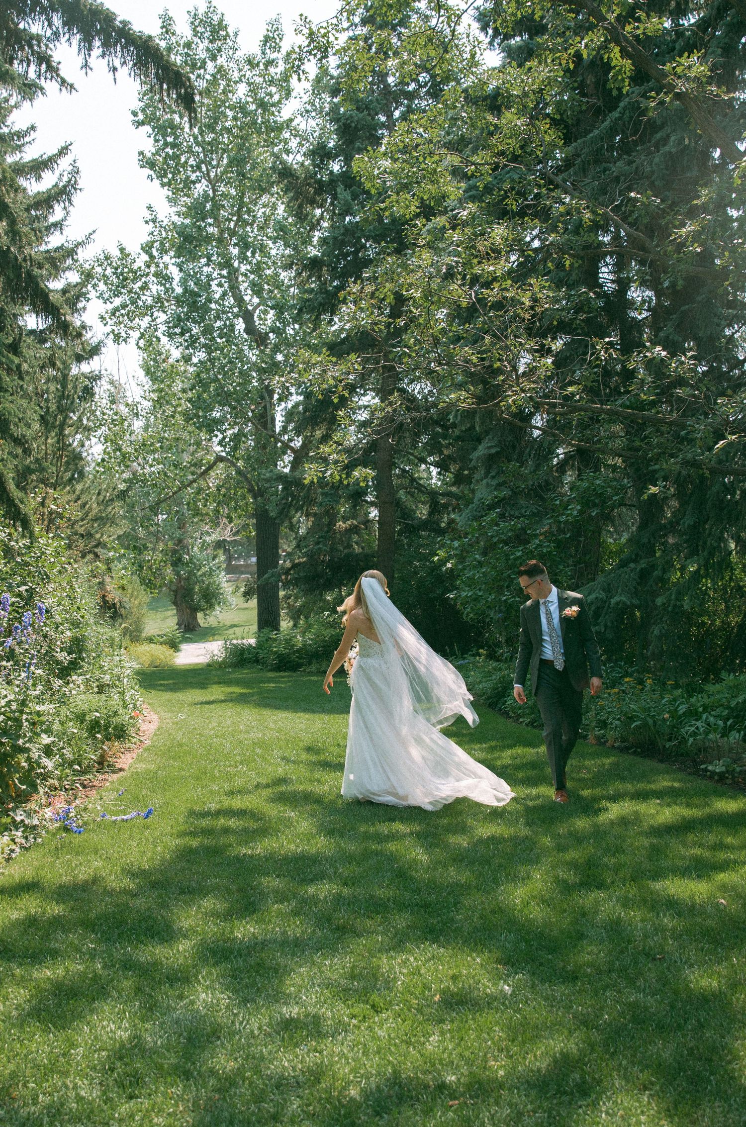 Bride and groom share a playful moment in a lush garden setting with flowing veil.