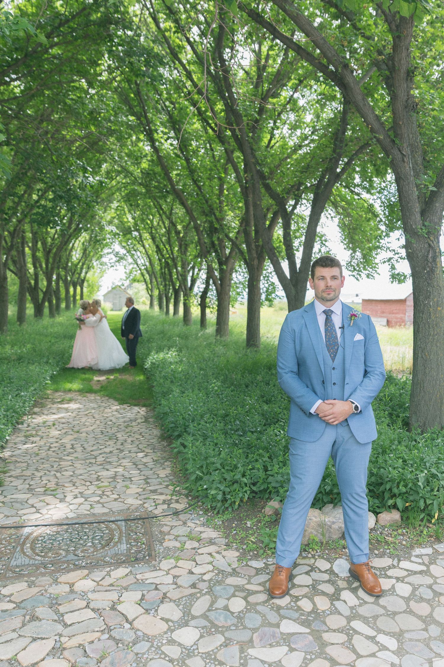 A cobblestone path winds through a green archway of trees during a wedding photo session.
