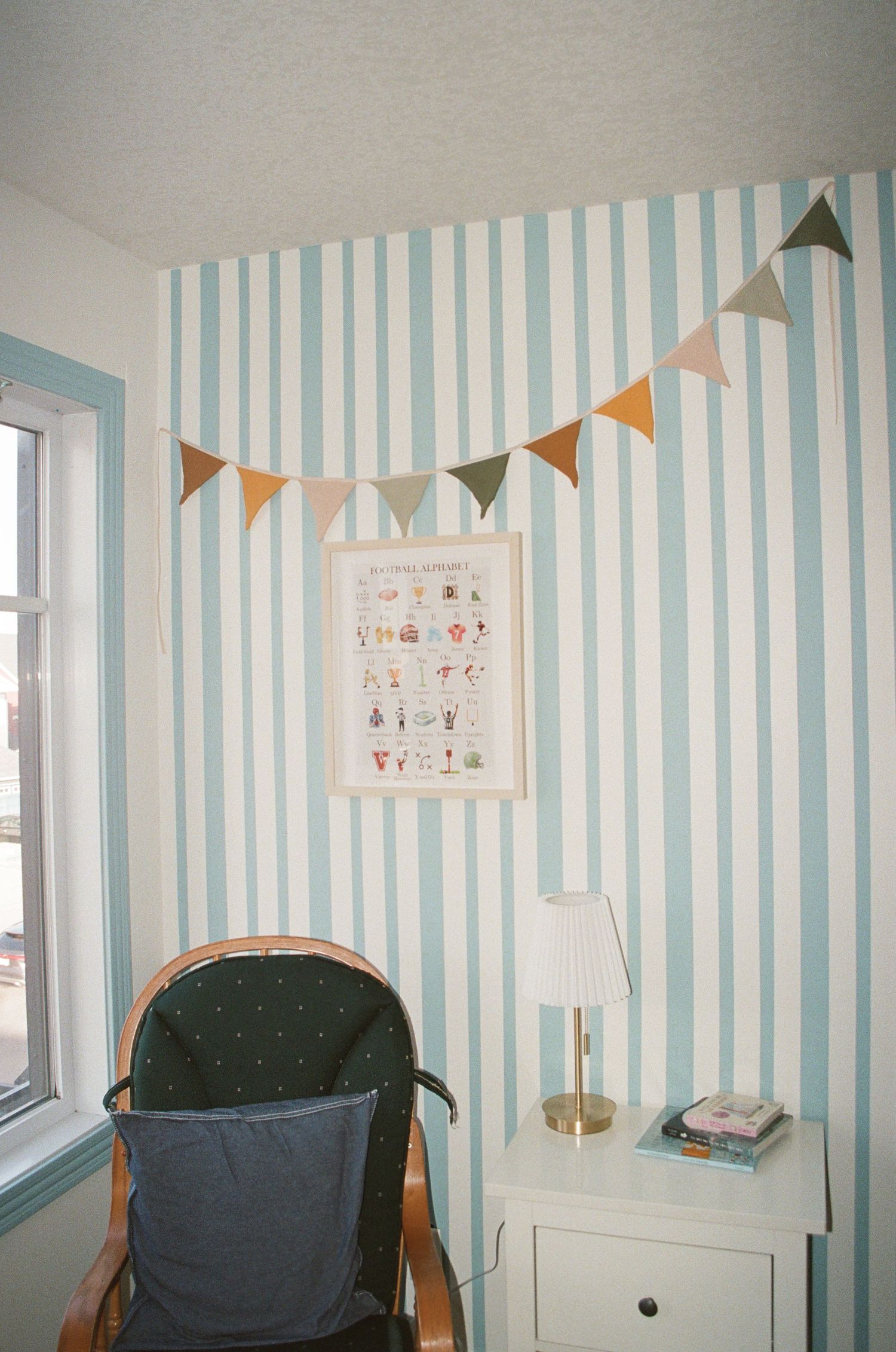 Blue and white striped wallpaper adorns a room with orange bunting flags and framed artwork on the wall.