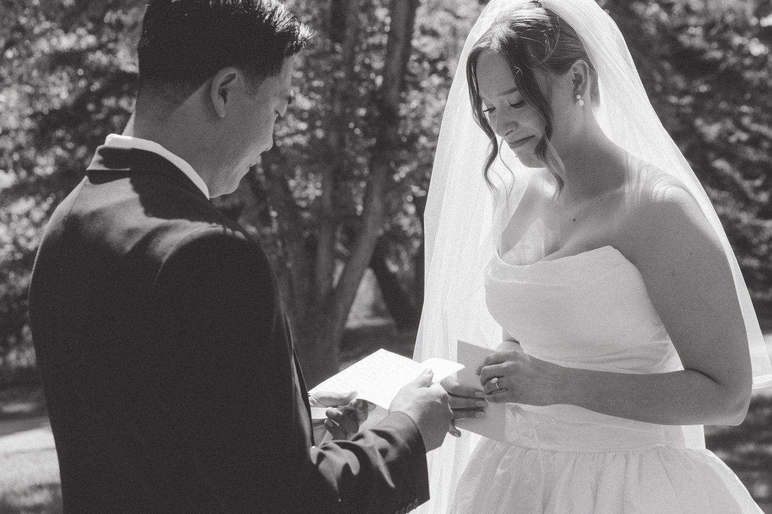 Black and white photo of a bride and groom exchanging rings during an outdoor wedding ceremony.