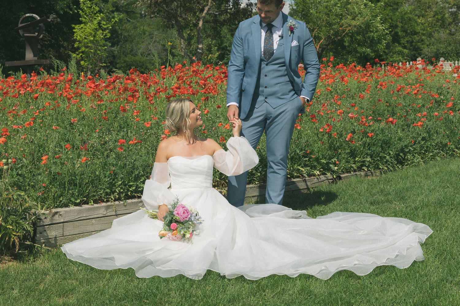 Wedding couple poses in a field of red poppies with flowing white dress.