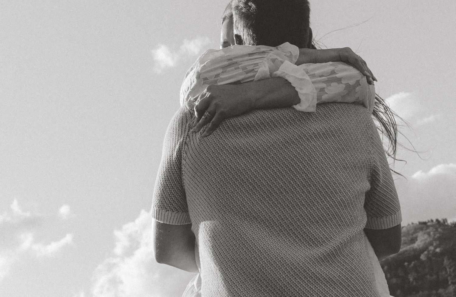 Black and white low-angle view of a person in sweater against bright sky with clouds on a sunny day.