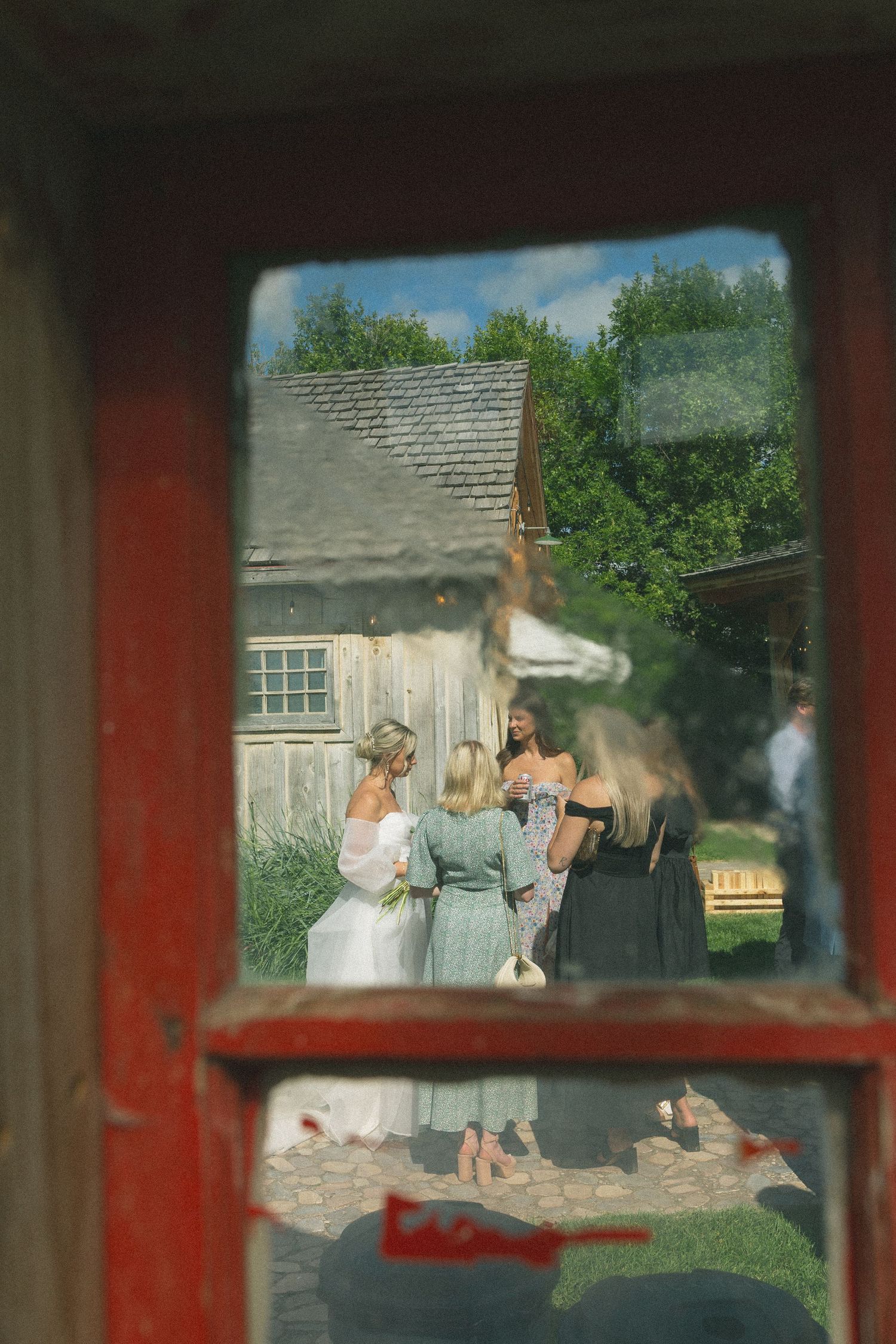 View through red window frame of outdoor wedding gathering.