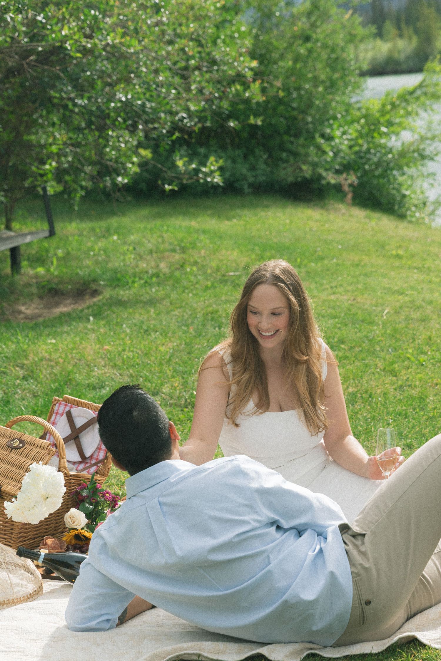 A couple having a picnic on a white blanket surrounded by lush green grass.