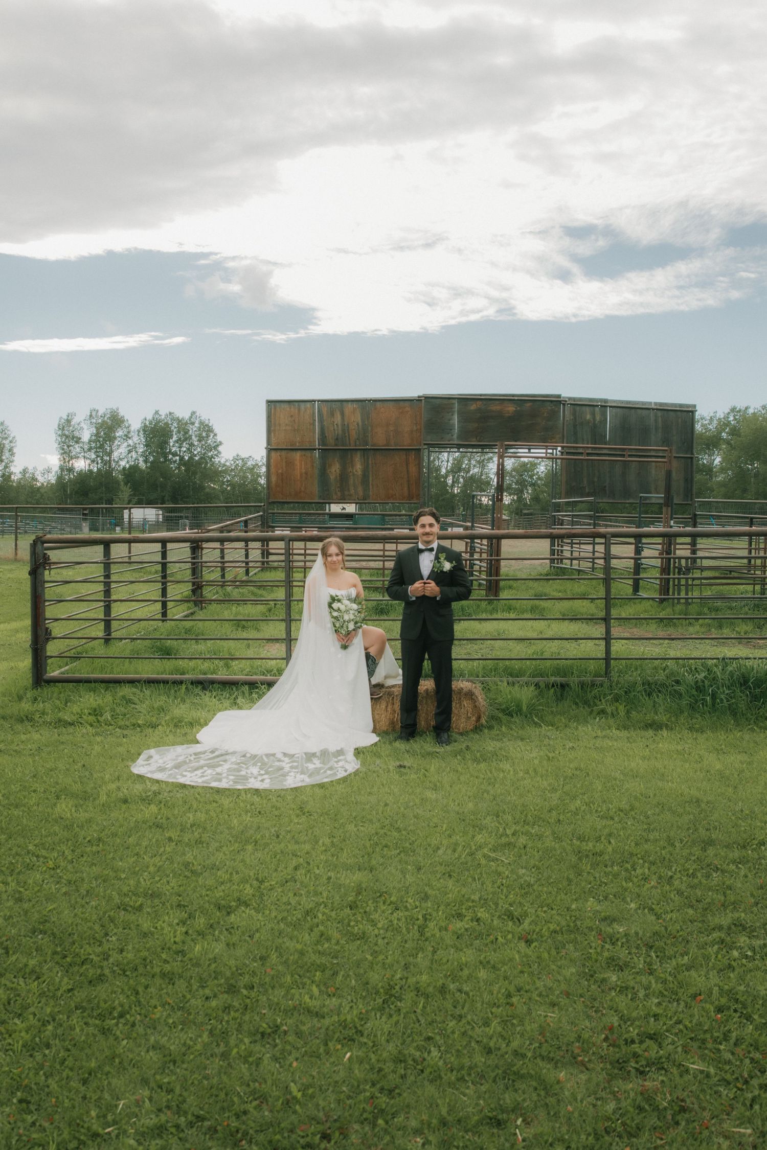 Bride and groom posing together in front of rustic farm fencing at an outdoor wedding venue.