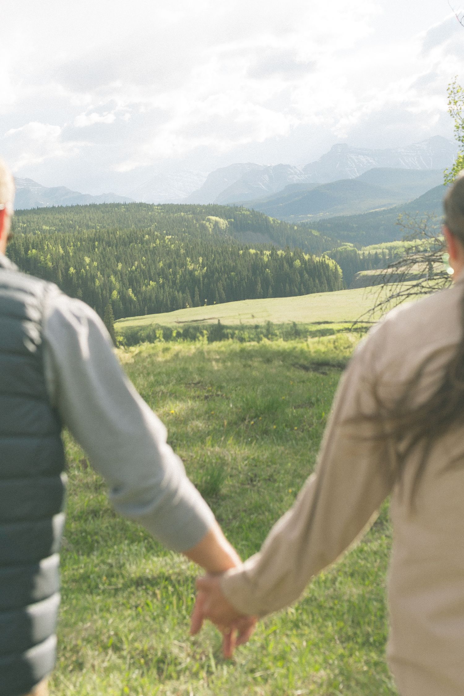 Couple holding hands while admiring breathtaking mountain valley views on a cloudy day.