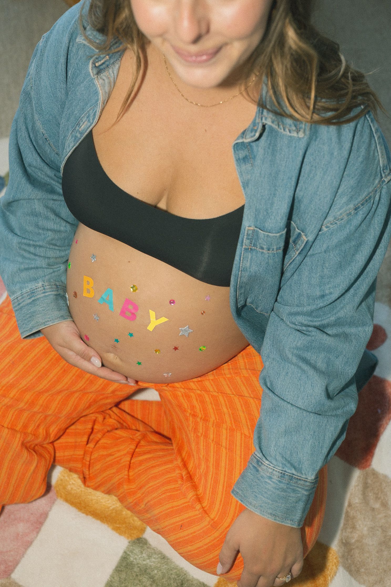 Close-up of torso wearing denim jacket and orange striped pants with colorful stickers on stomach.