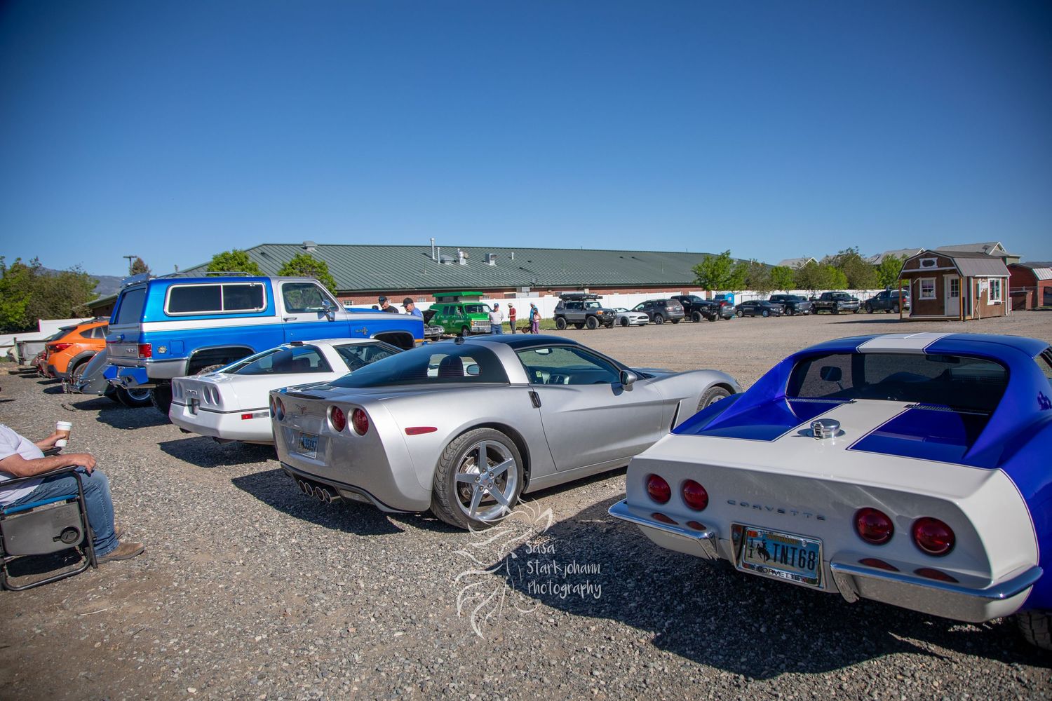 Classic Chevrolet Corvettes and other sports cars parked in a row at an outdoor car show gathering on gravel lot.