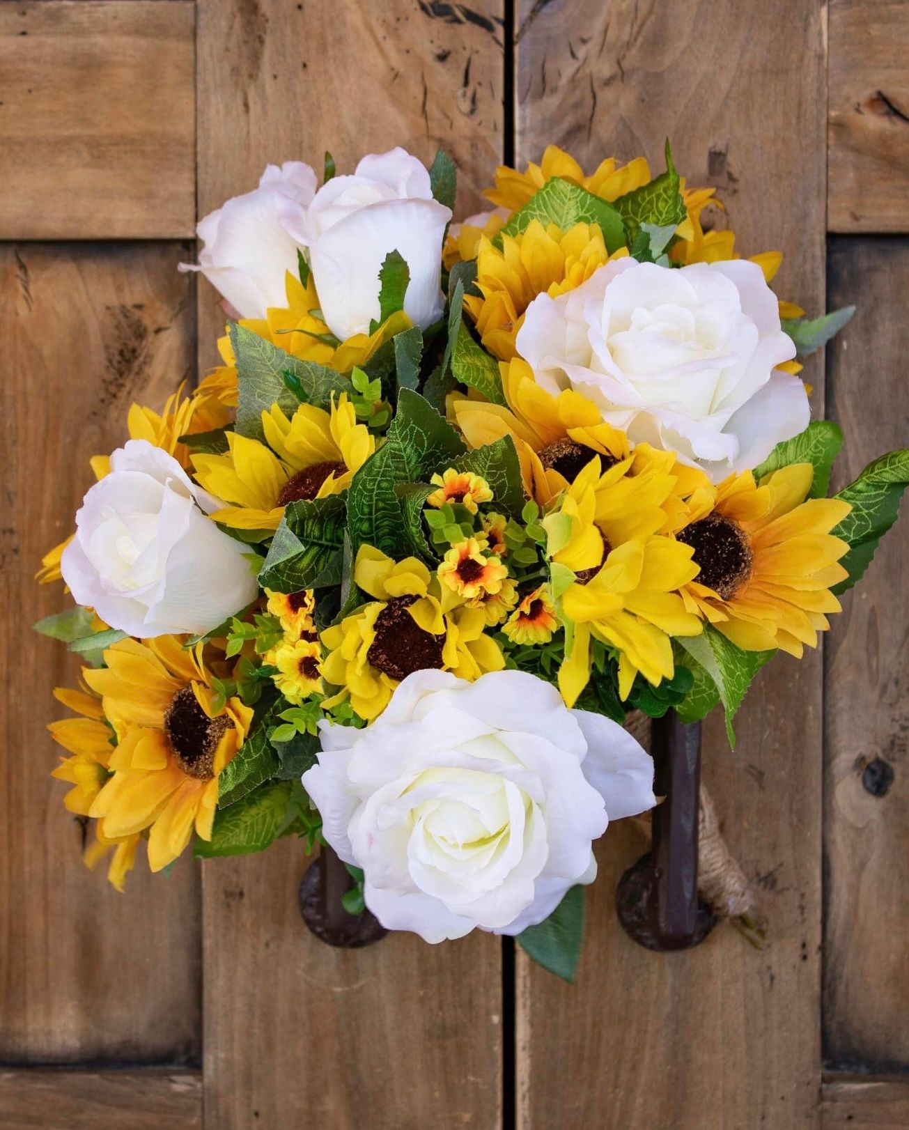 Beautiful floral arrangement combining white roses and bright yellow sunflowers against rustic wooden background.