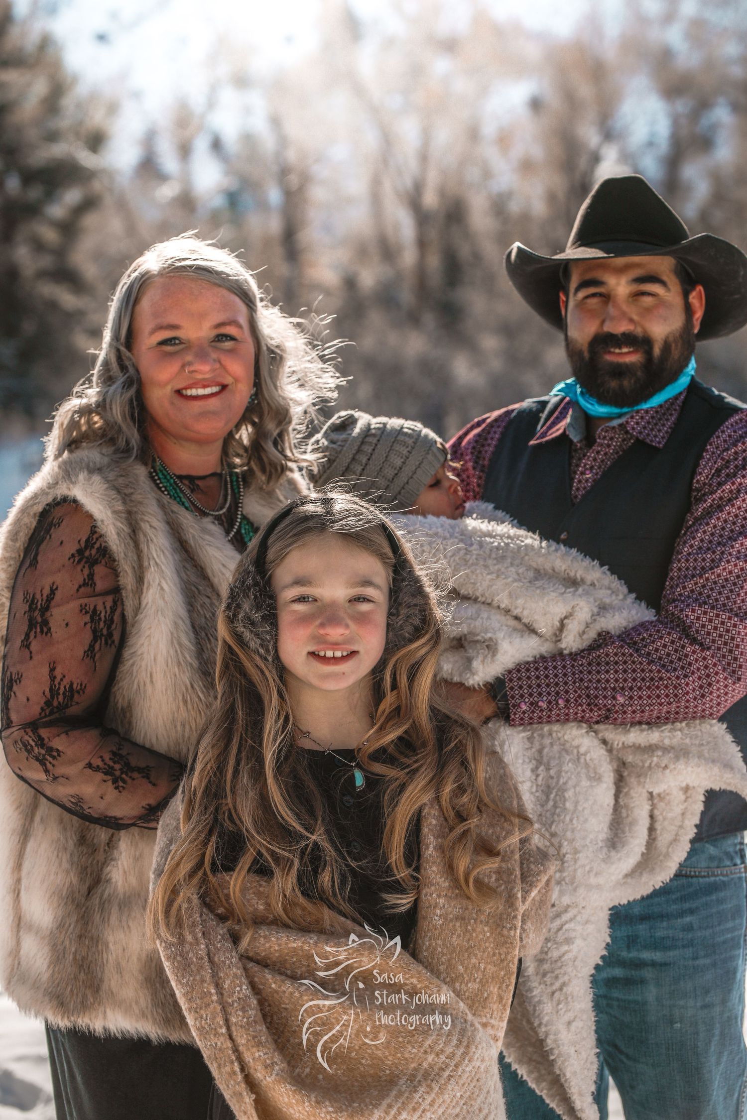 A family group poses outdoors in western wear and cozy winter clothing against a snowy backdrop.