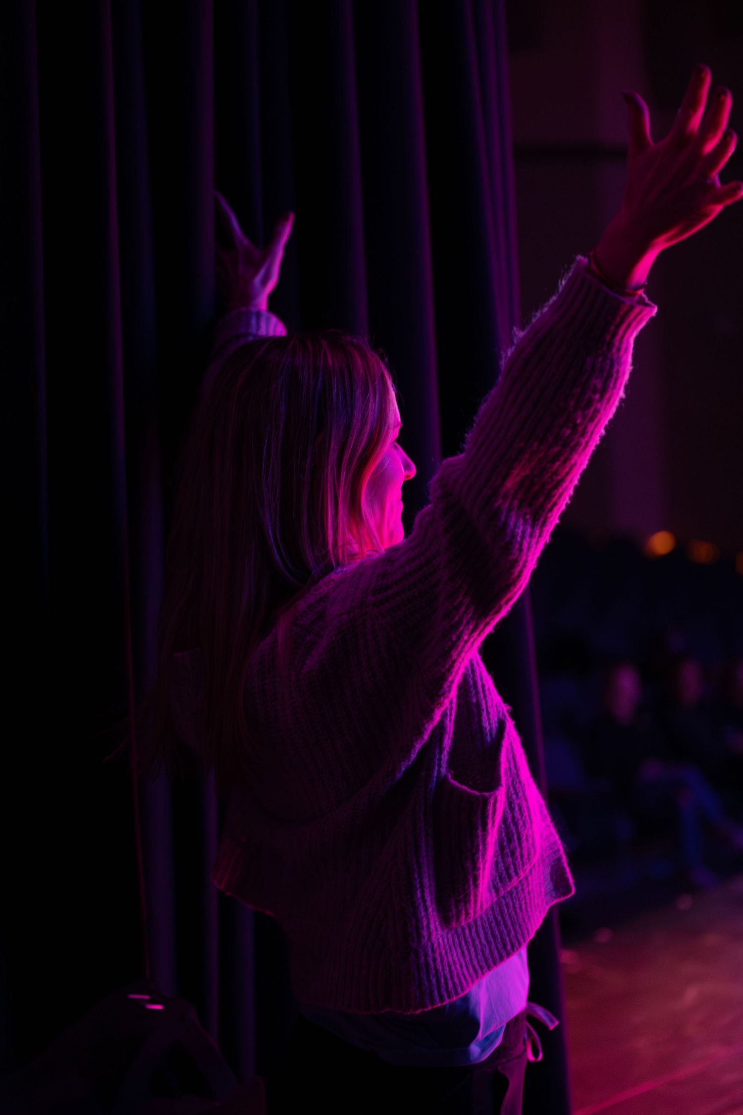 Silhouette of performer raising arms in purple stage lighting during theatrical performance.