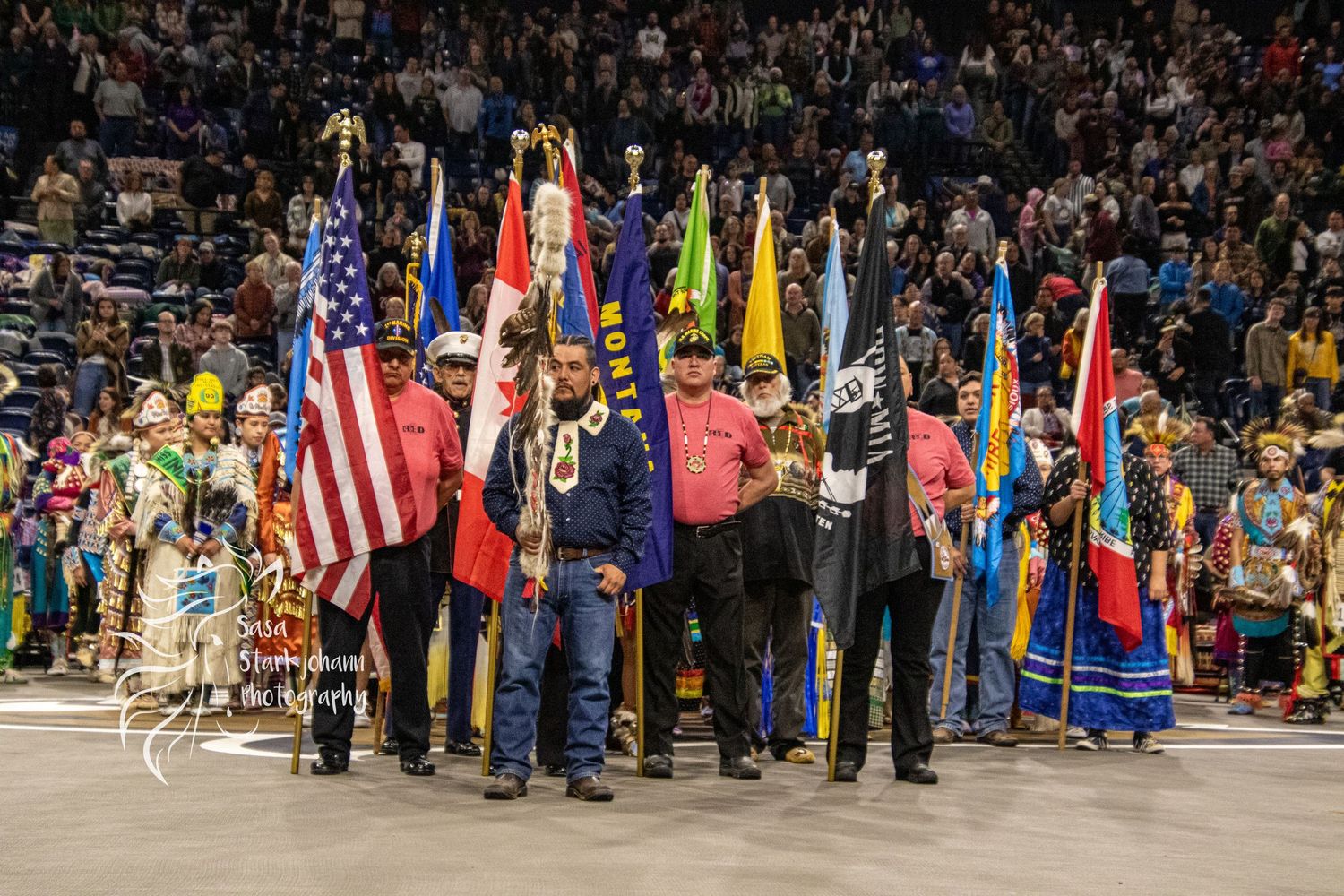 Color guard presenting flags at Native American cultural celebration with crowd in background.
