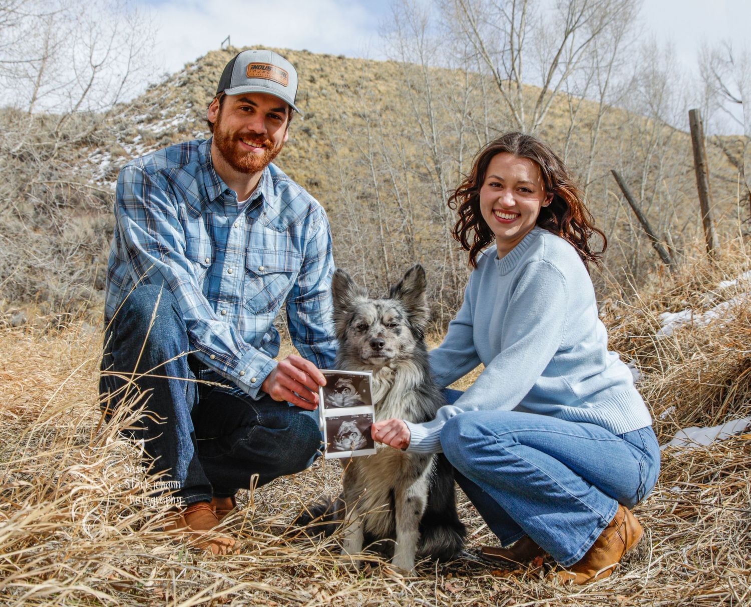 Couple and their dog sharing ultrasound photos in outdoor pregnancy announcement.