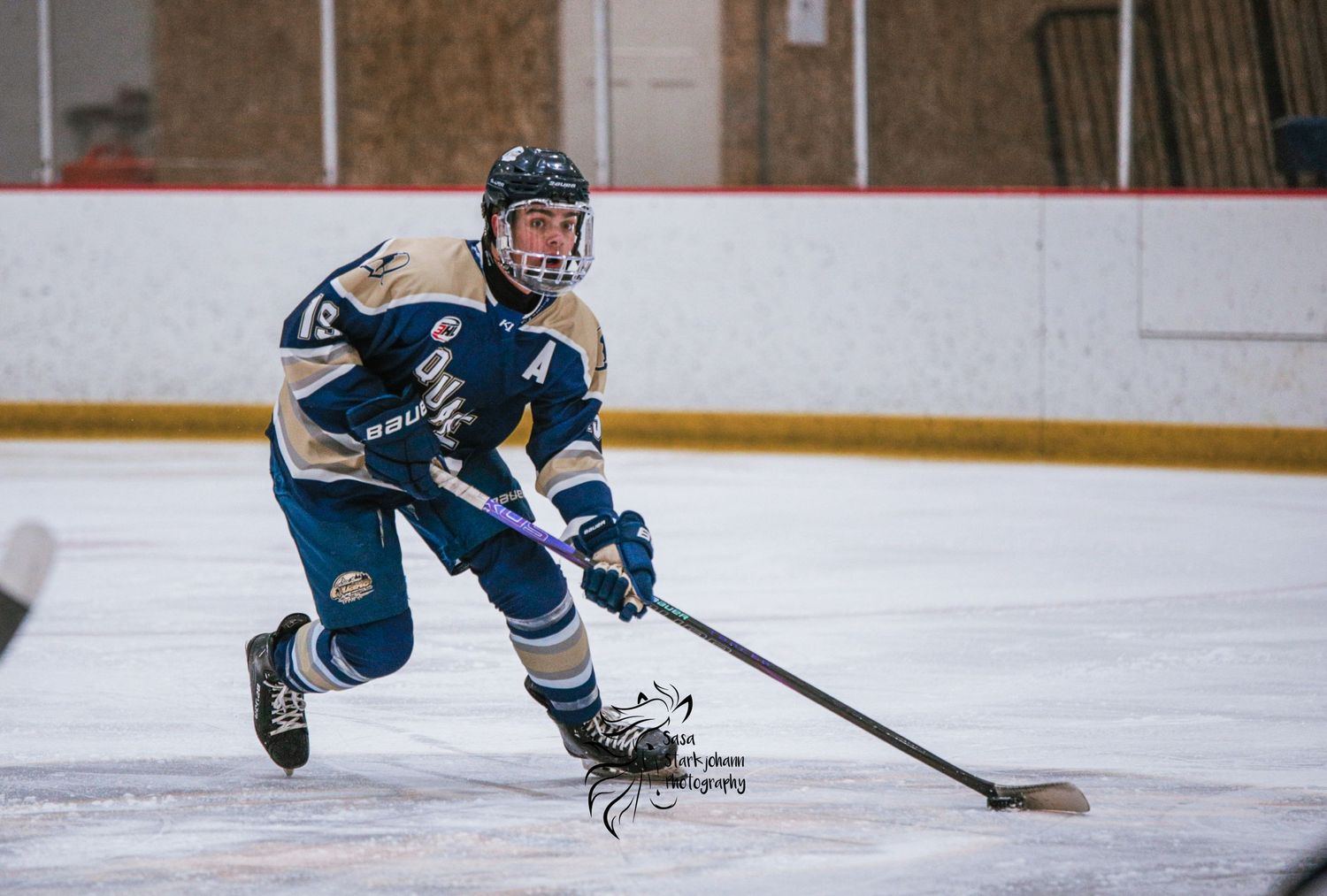 Hockey player in blue jersey skates with puck during intense game action.