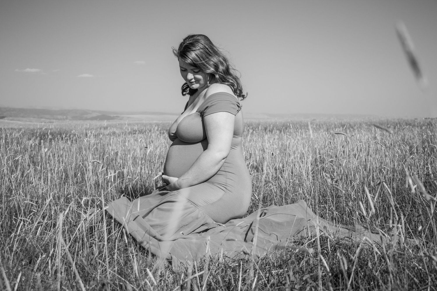 Artistic maternity photo of an expectant mother sitting in a wheat field.