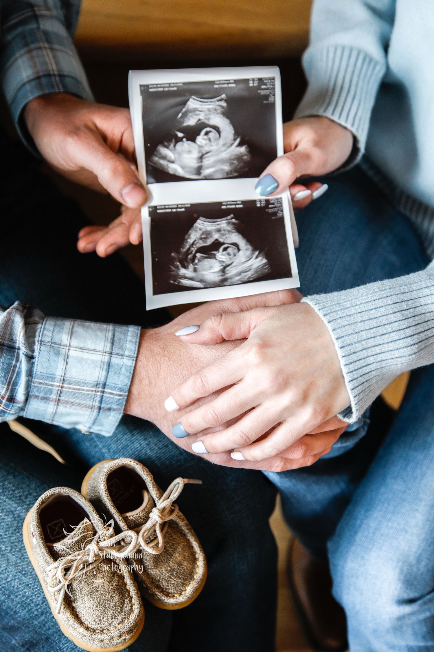 Hands holding ultrasound photos next to tiny baby shoes in a pregnancy announcement photo.