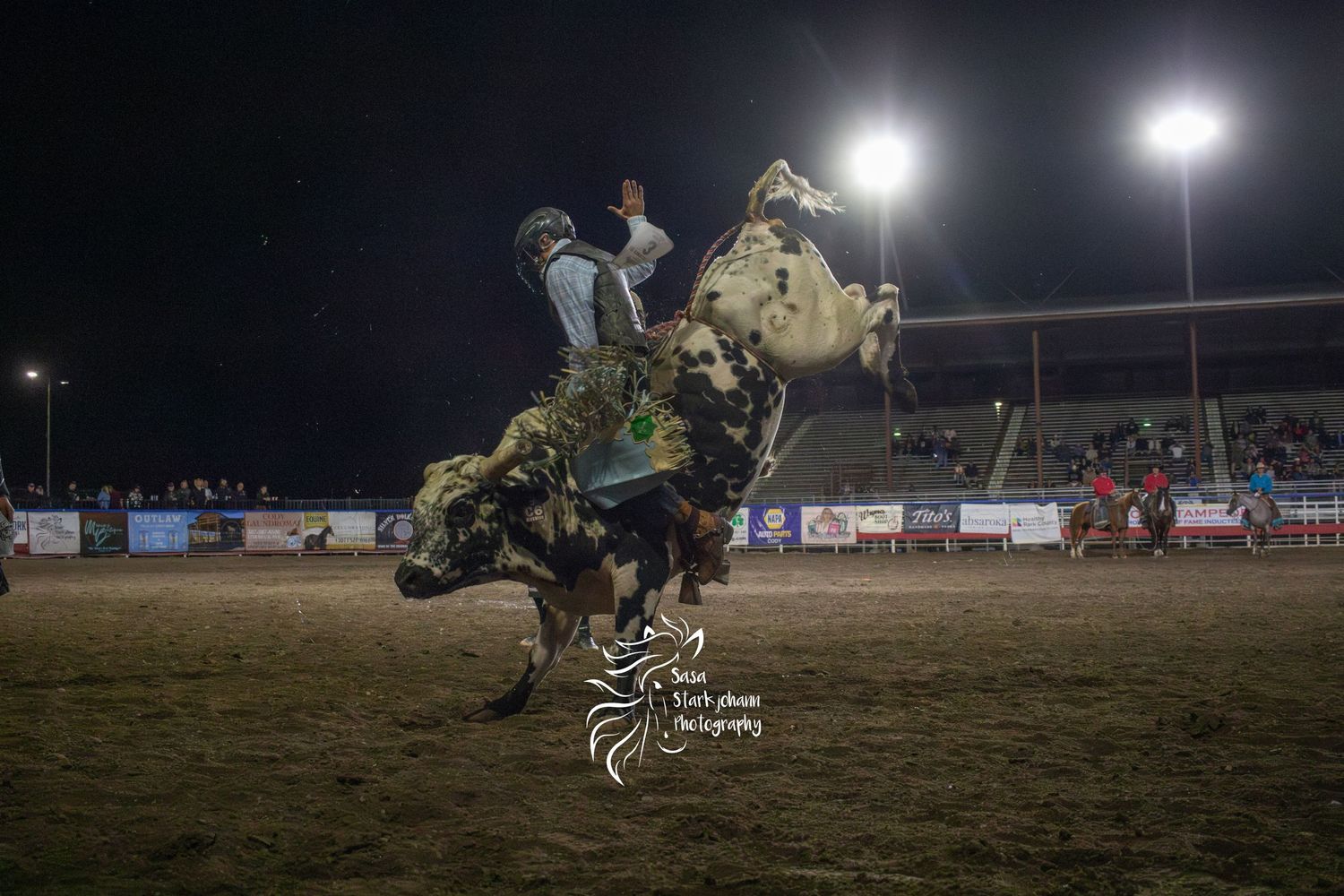 Rodeo rider on bucking bronco under bright stadium lights at night event.