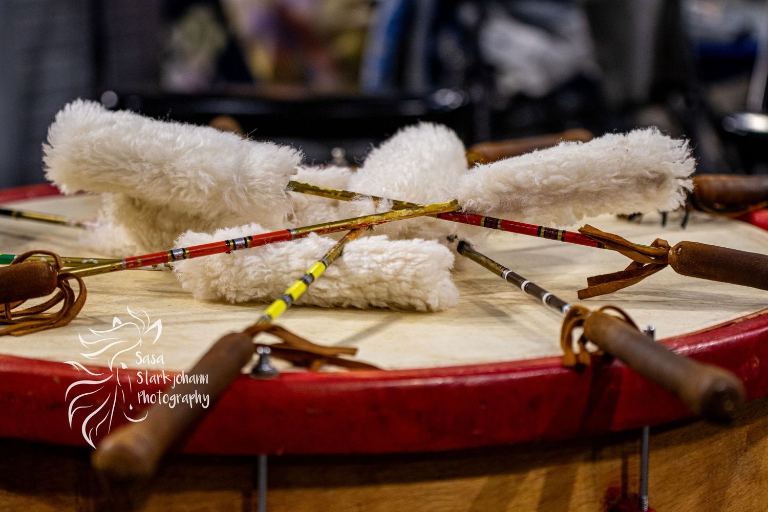 Traditional Native American drum sticks with white fur displayed on red drum surface.