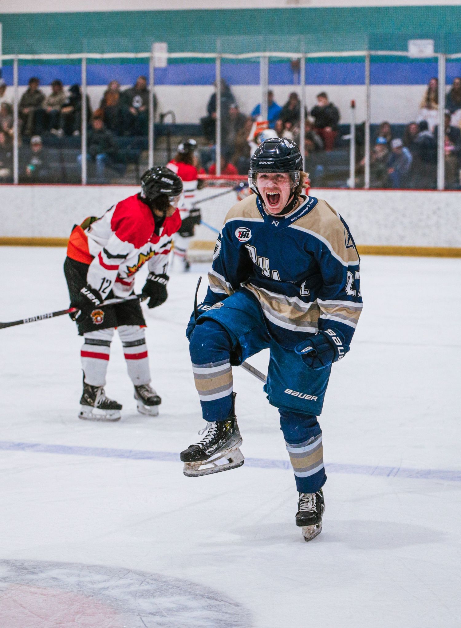Hockey player celebrating on ice during an indoor game with spectators in background.