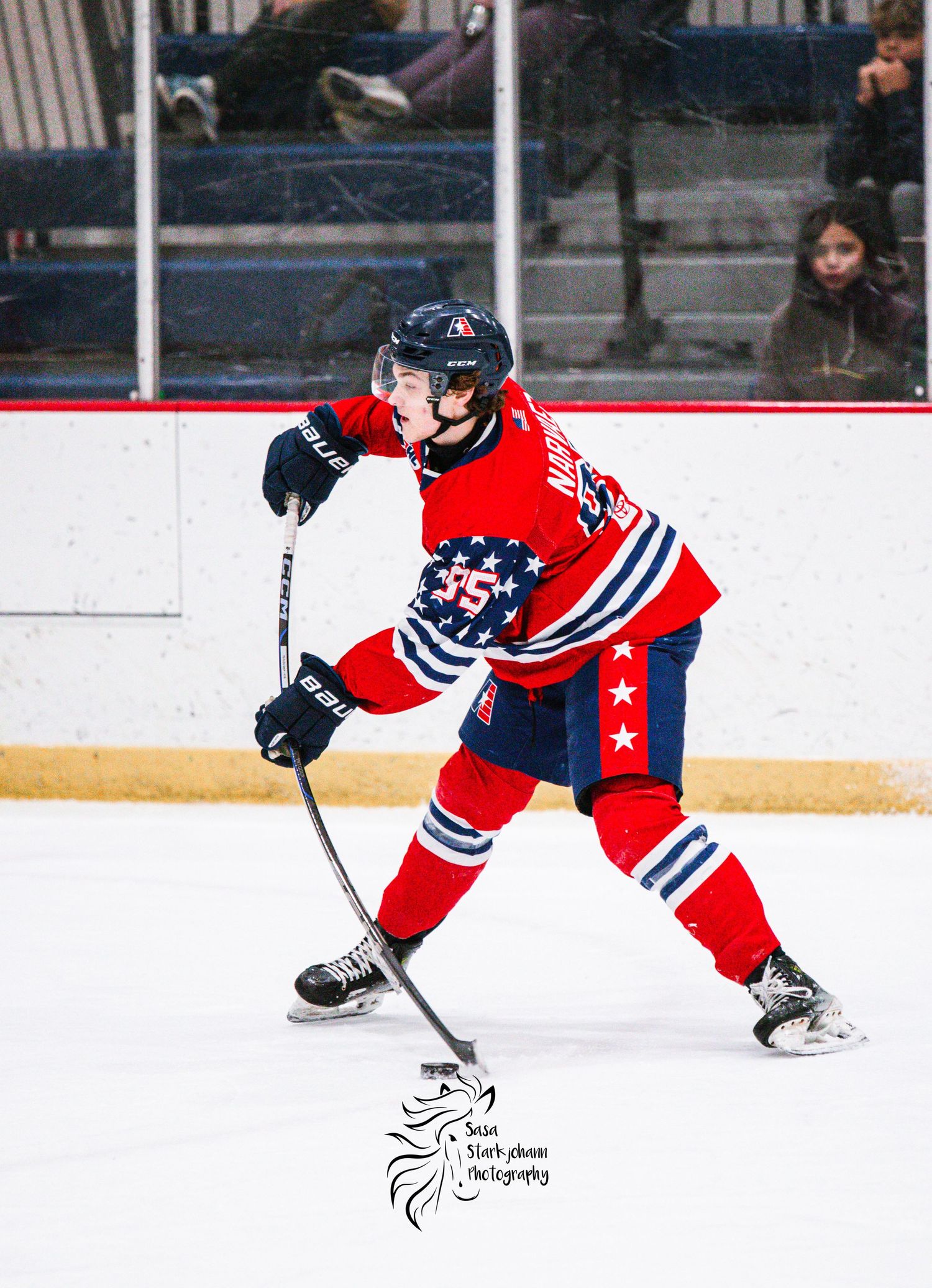 Hockey player in red and blue jersey with stars practicing on ice rink.