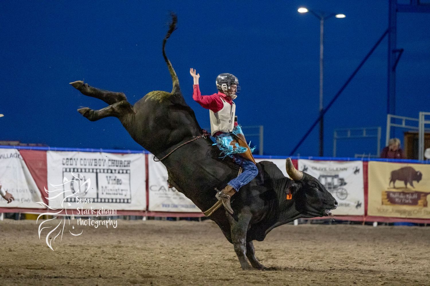 A bull rider performs at a rodeo competition under night lights.