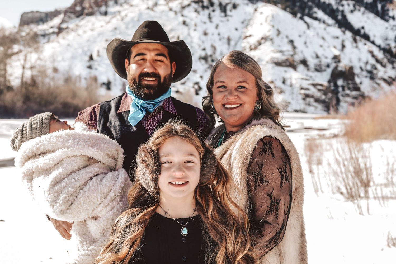 Winter family portrait in western attire against snowy mountain backdrop.
