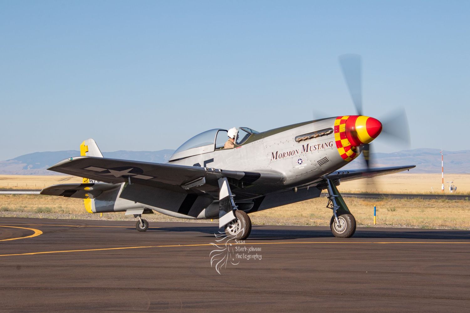 Vintage P-51 Mustang warbird with distinctive red nose parked on desert airfield under blue sky.