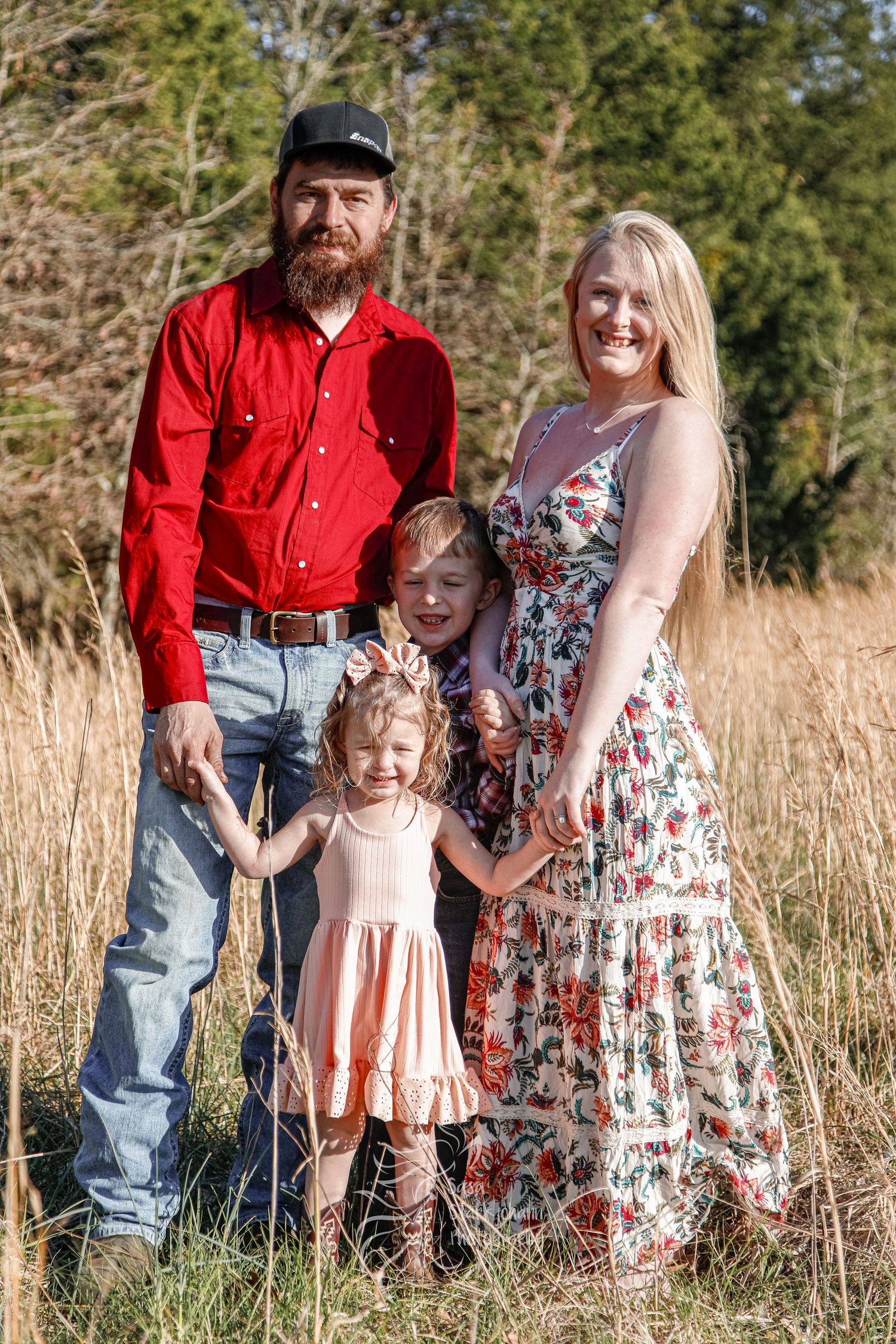 Family poses together in a field wearing coordinated outfits with floral dresses and casual attire.