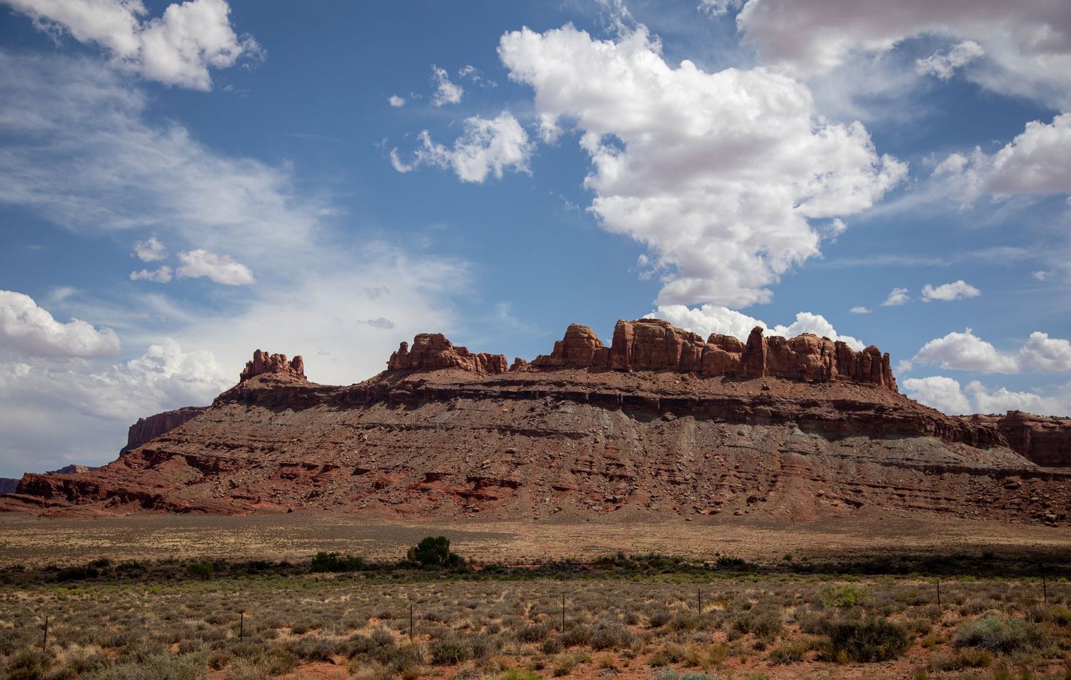 Majestic red rock formations rise against a blue sky with puffy white clouds in Utah's desert landscape.