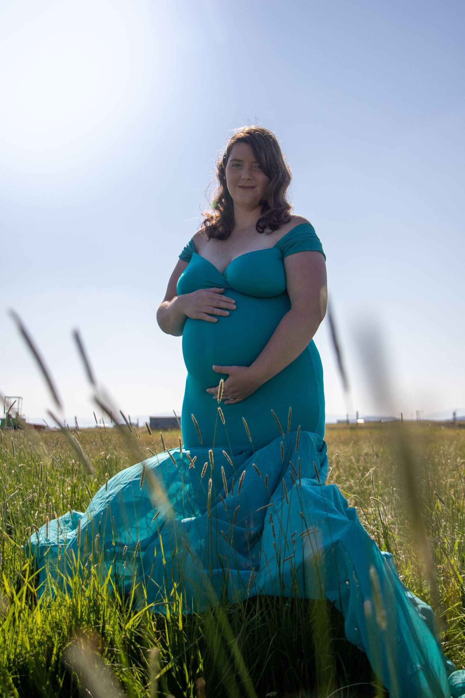 Maternity portrait in a teal gown amid sunlit grass field.