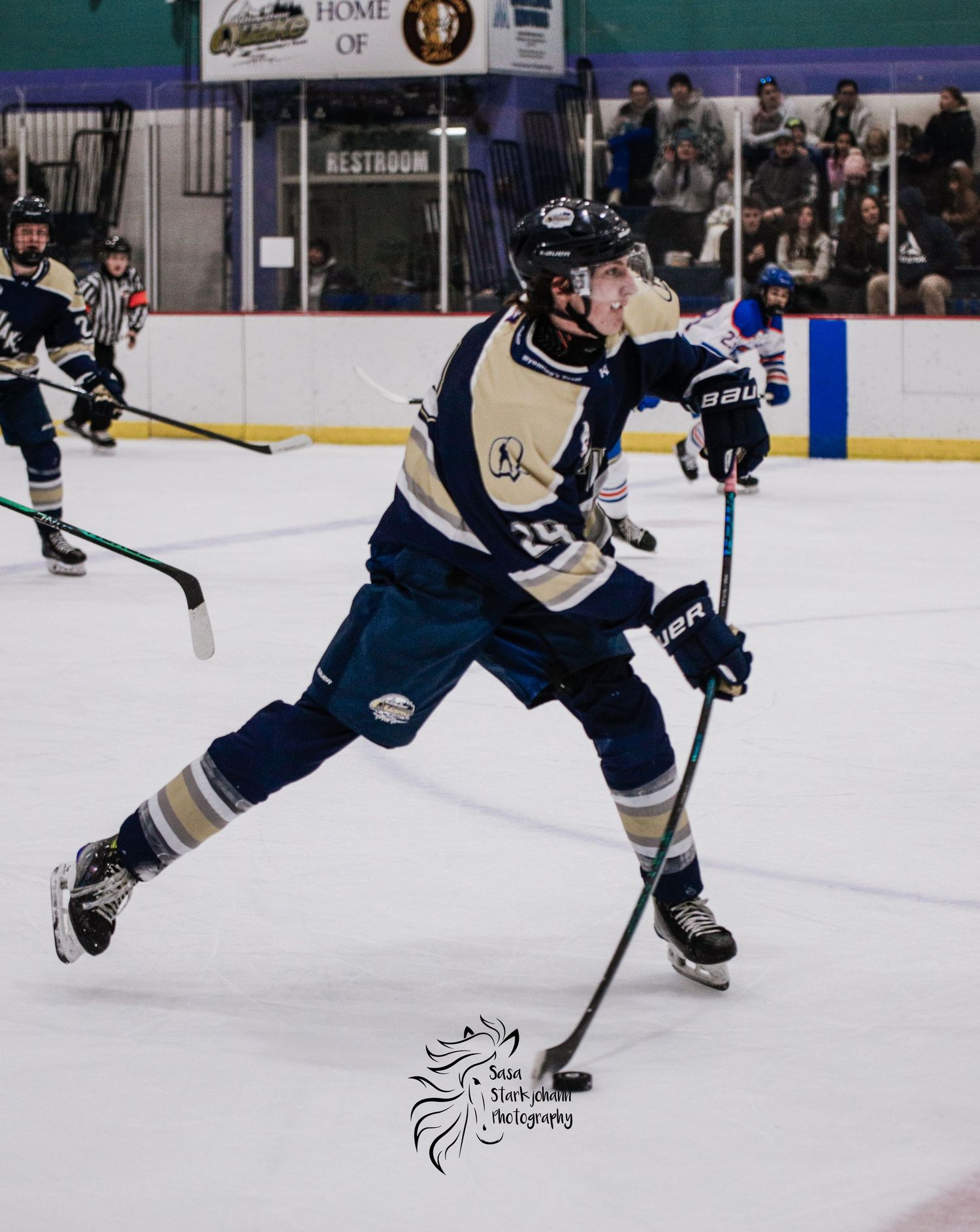 Hockey player in navy uniform takes powerful shot while skating on ice rink.