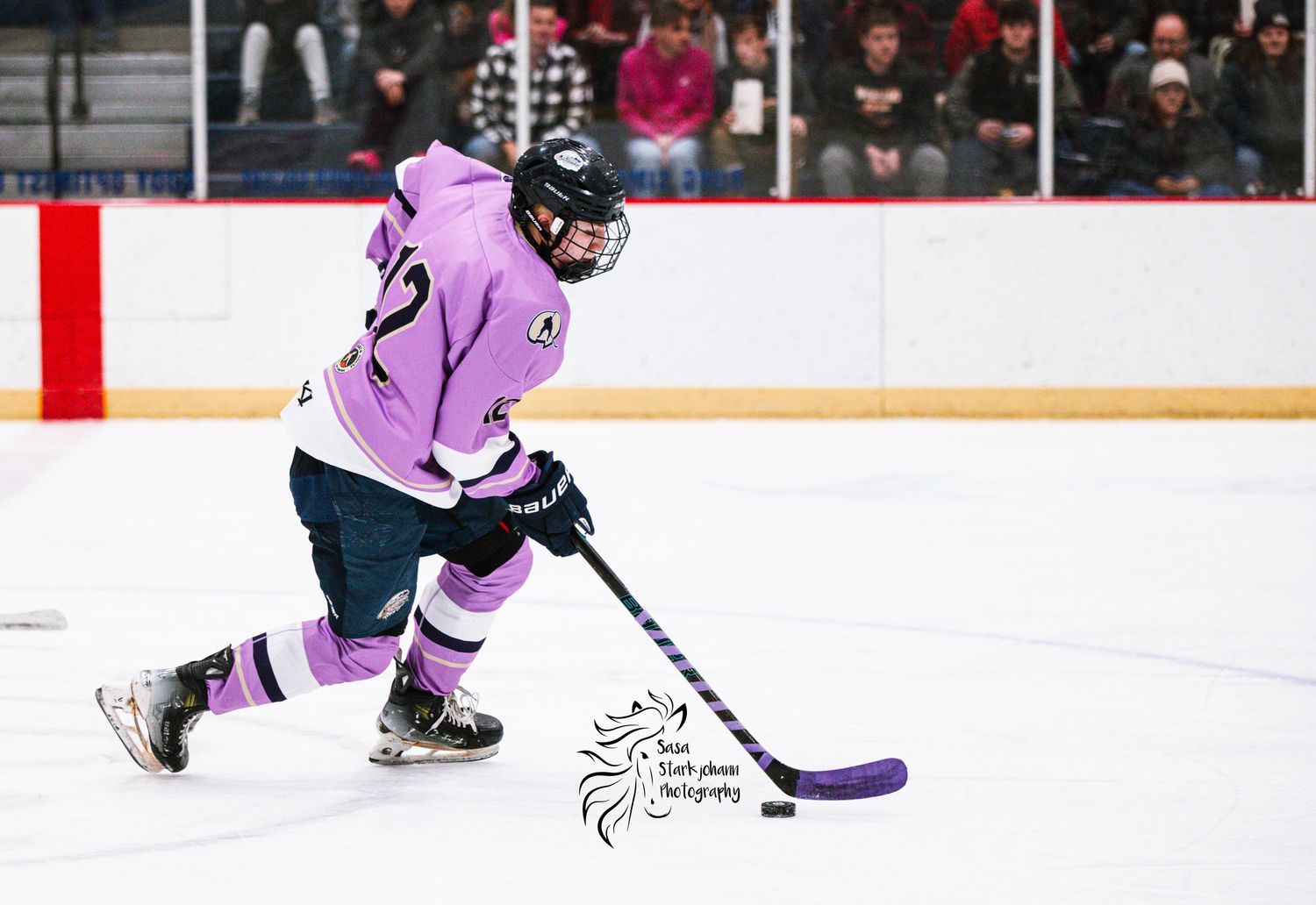 Ice hockey player in pink jersey handles puck while skating on rink.