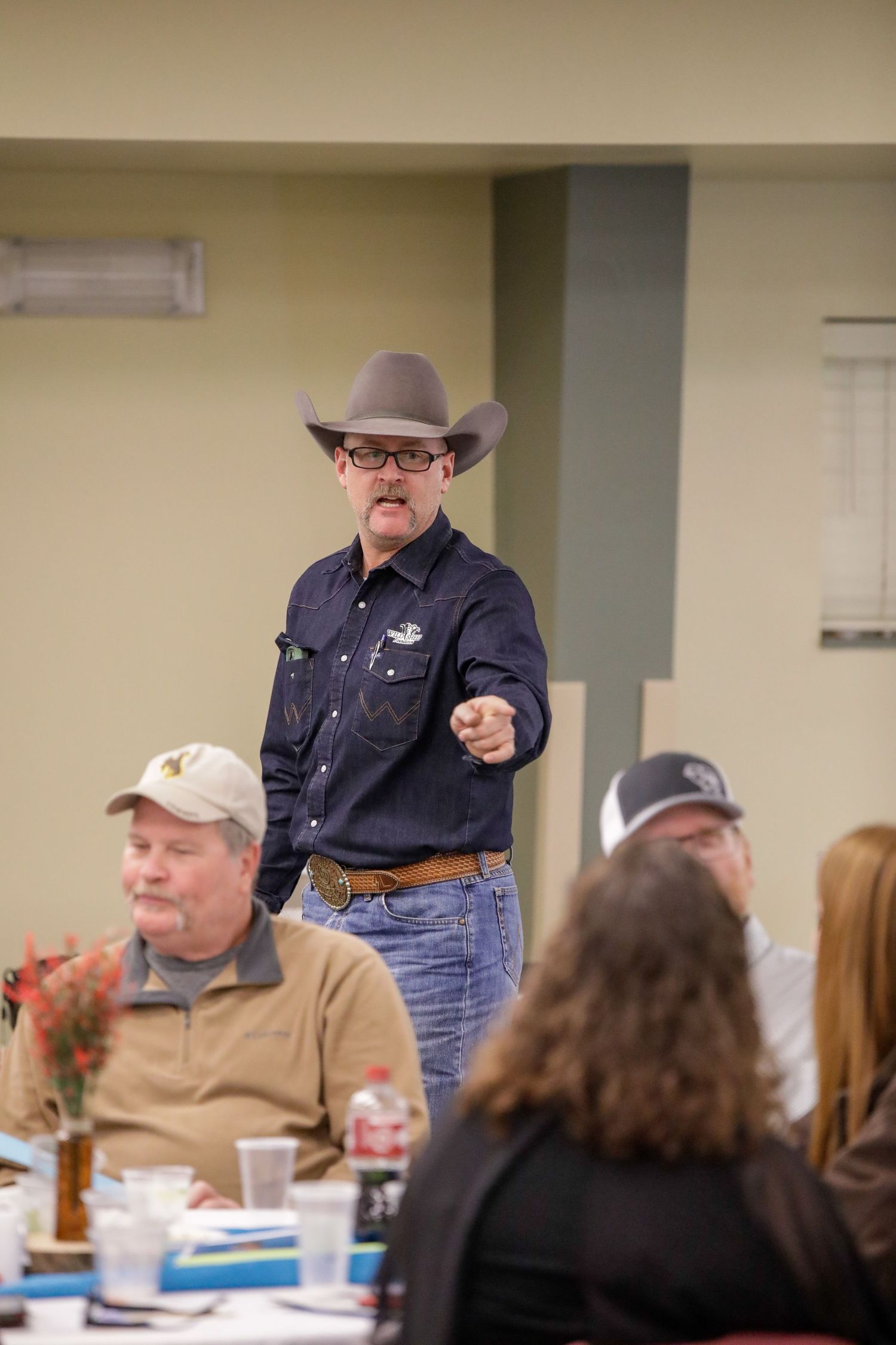 Speaker in western attire addressing audience during indoor community event.