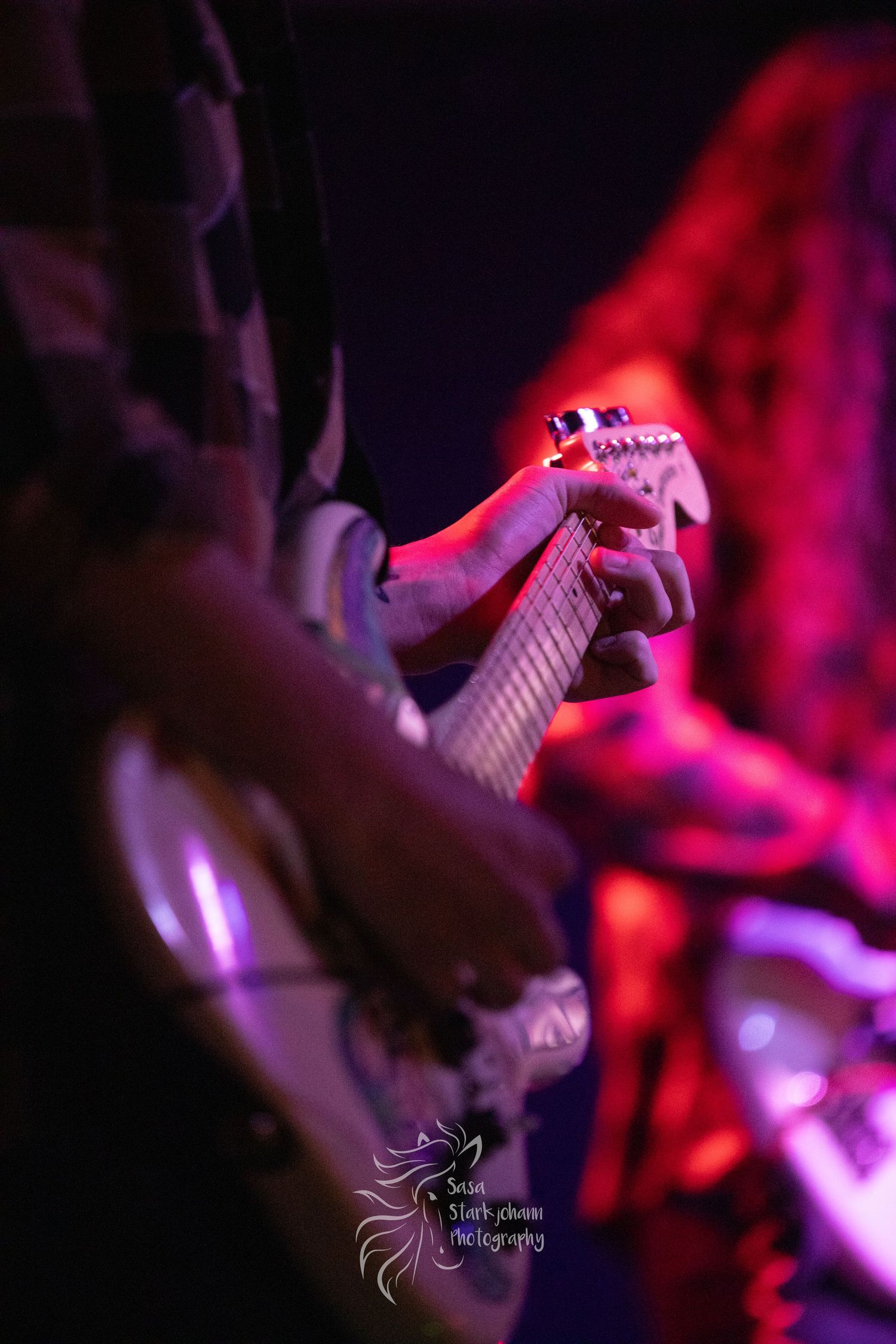 Close-up shot of hands playing electric guitar under dramatic red stage lighting.
