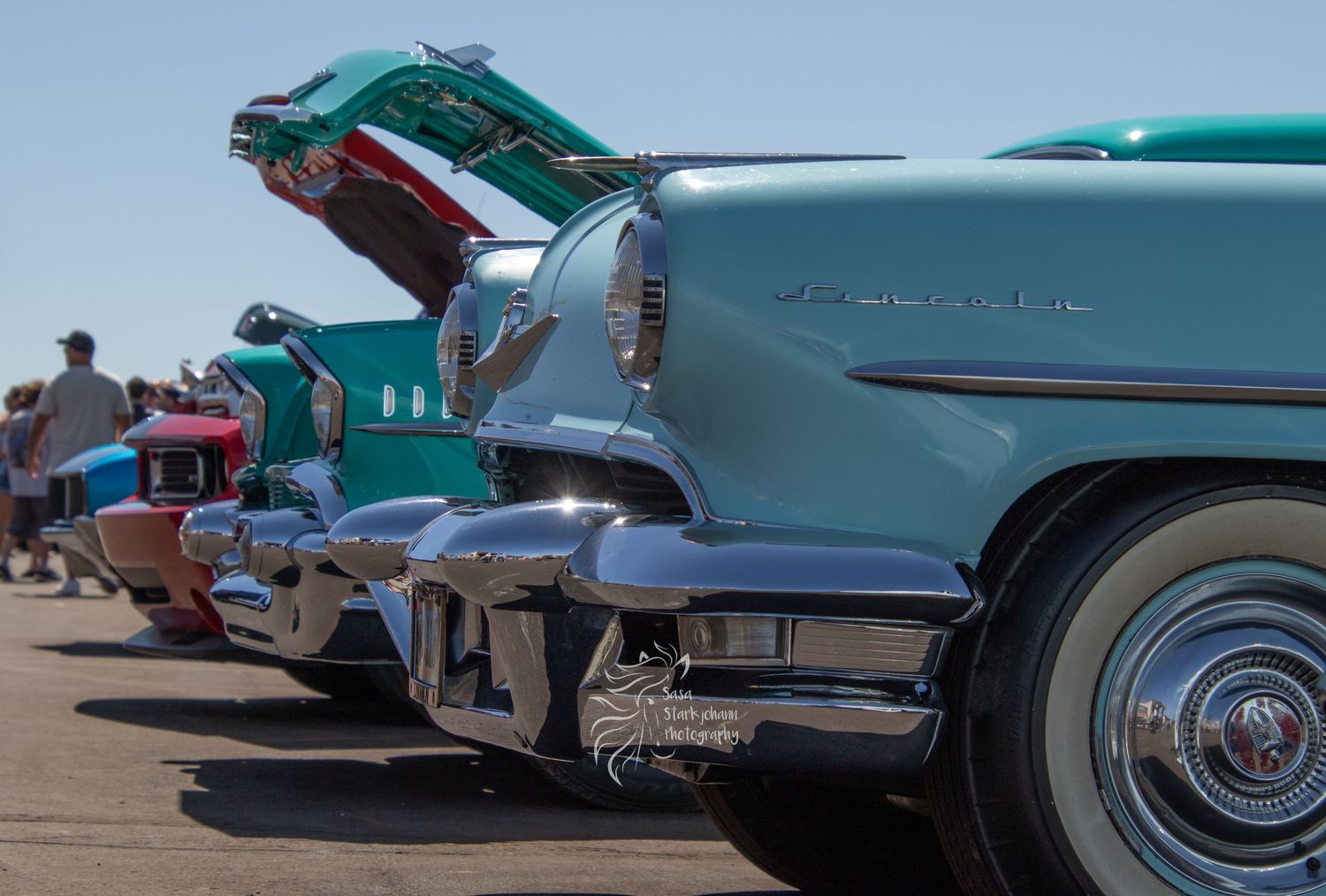 Row of classic 1950s turquoise cars with fins displayed at outdoor car show.
