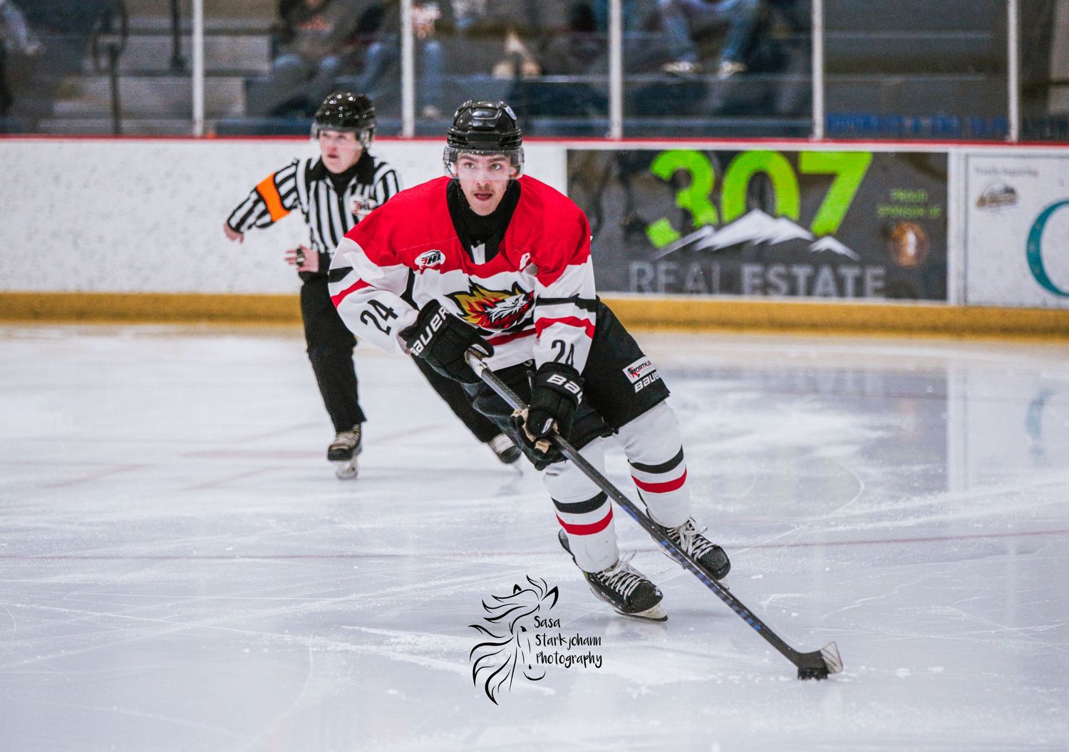 A hockey player in red jersey skates with the puck during an indoor game.