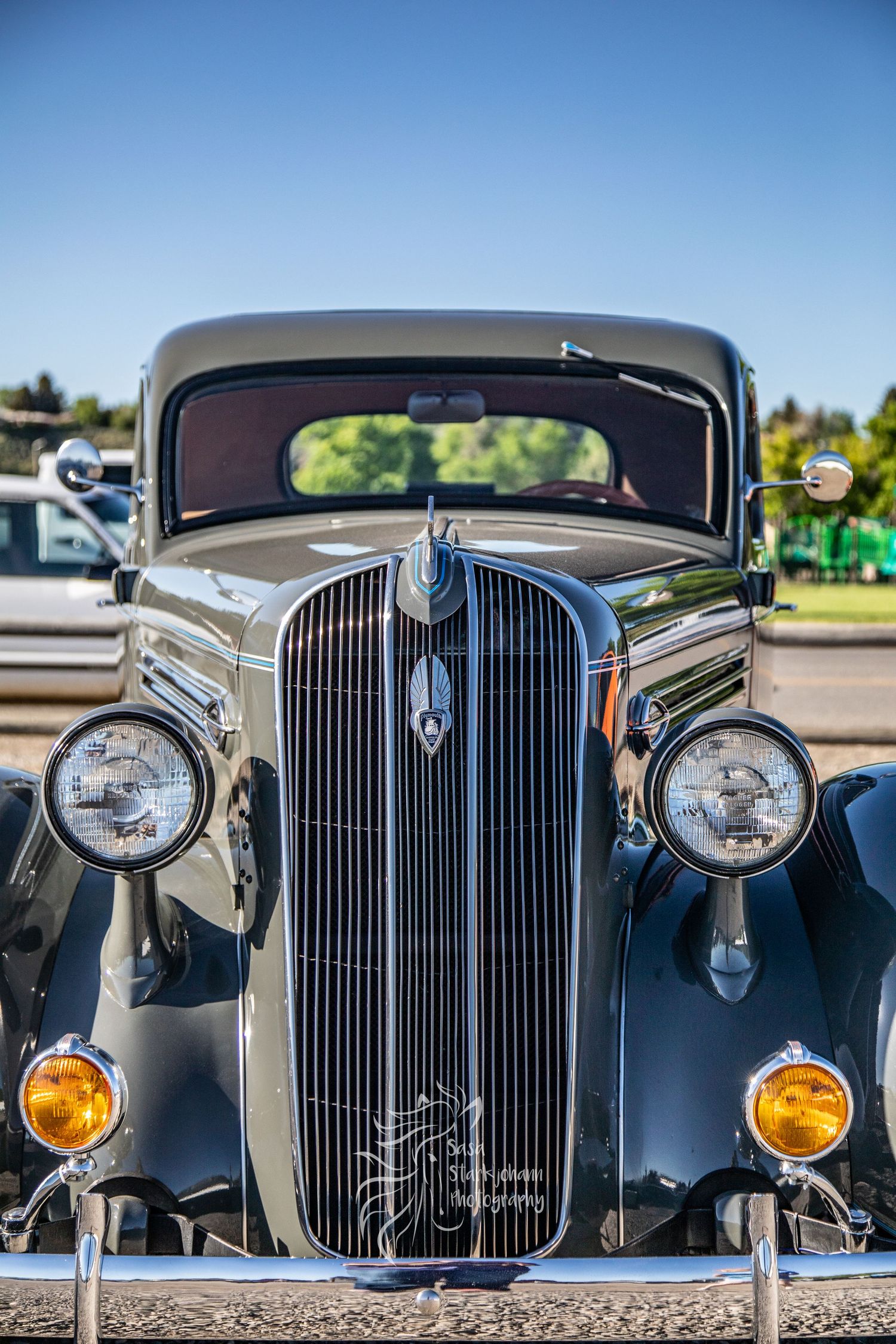 Front view of a vintage 1930s car showing classic vertical grille, round headlights and amber fog lights against blue sky.