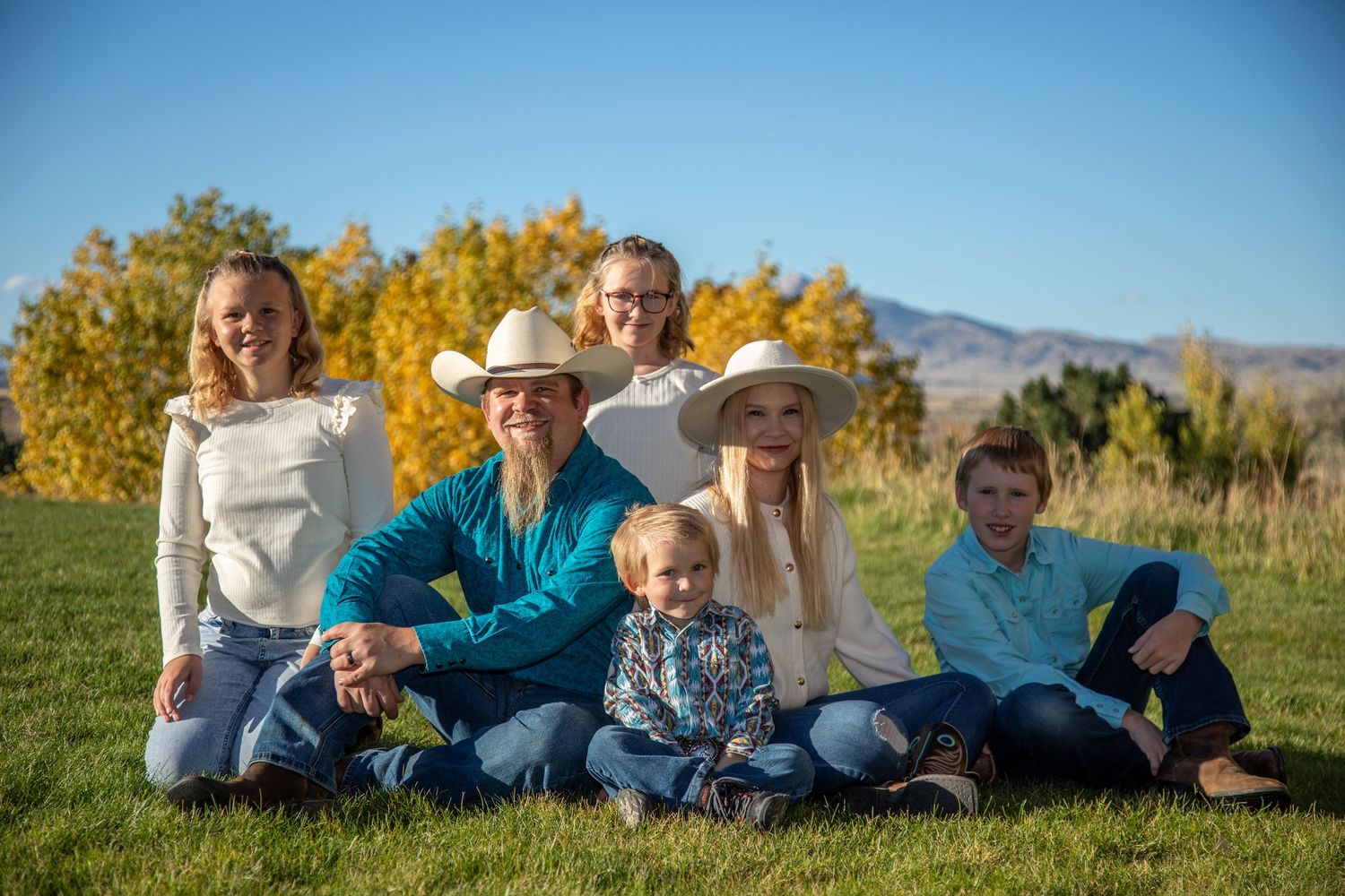 Family members lying together on grass with autumn foliage and mountains in background during outdoor photo session.