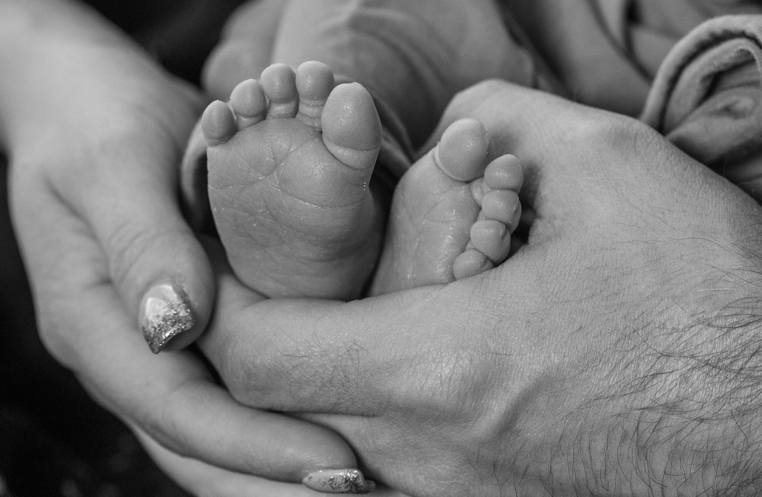 A series of black and white close-up photographs showing tiny newborn baby feet being held in adult hands.