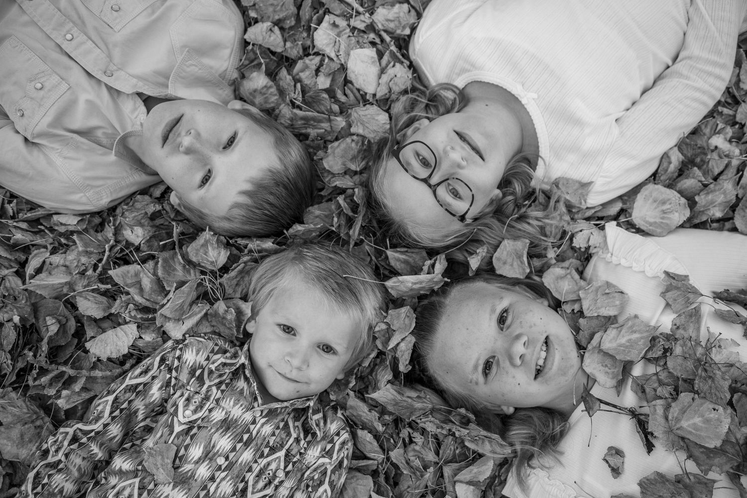 A series of black and white photos showing people lying in fallen autumn leaves on the ground.