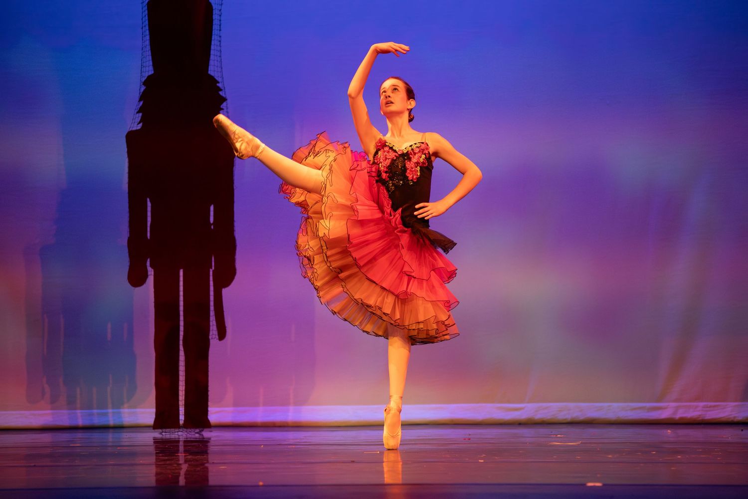 Ballet dancer in red dress performs elegant pose on stage with dramatic lighting.