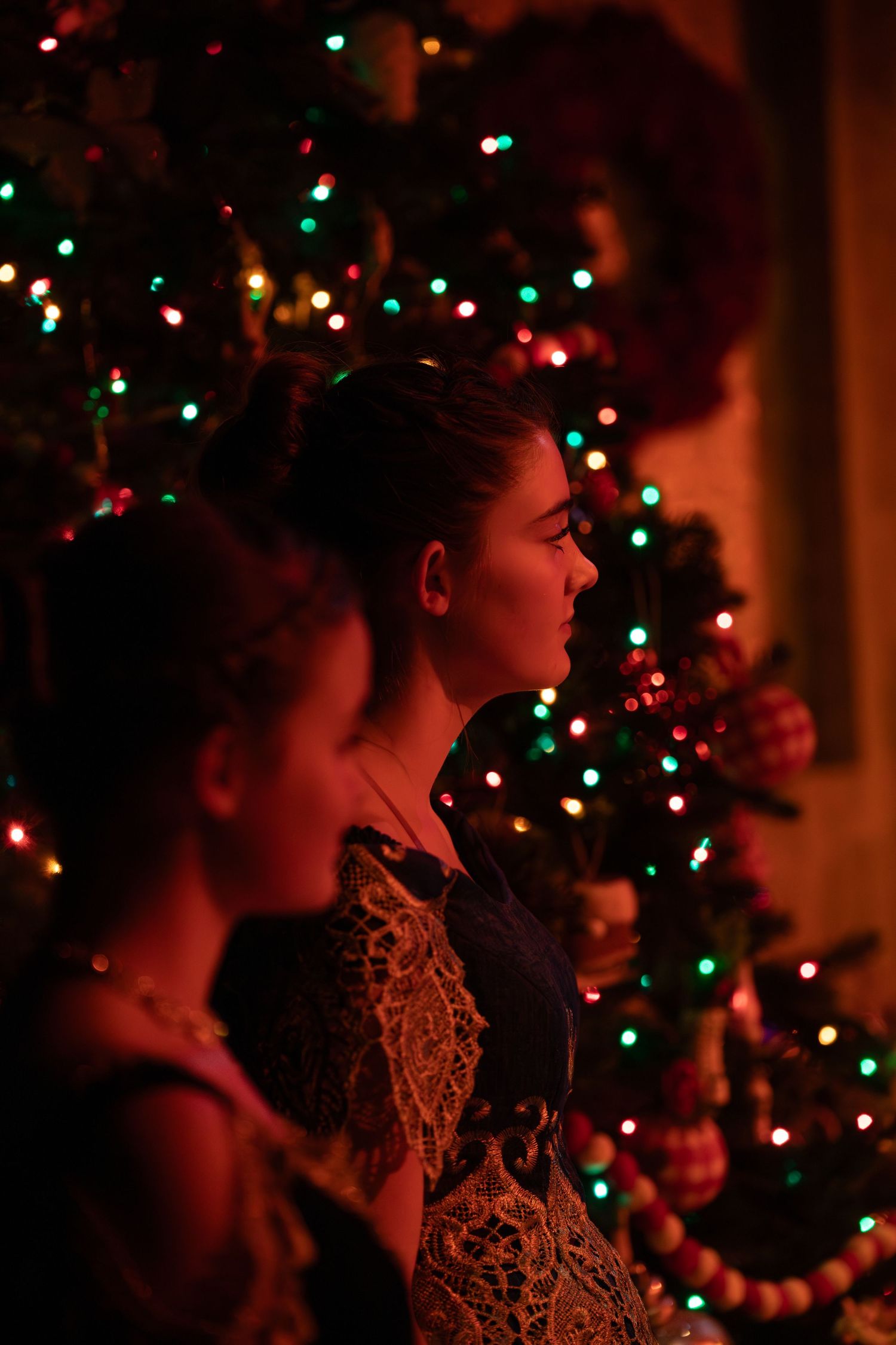 The profile of performers against a blurred Christmas tree with twinkling red and green lights.
