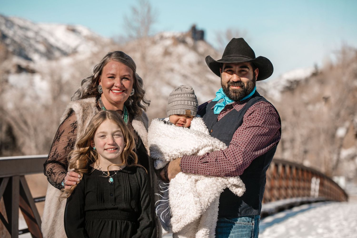 Happy family with young daughter posing on mountain bridge in winter.