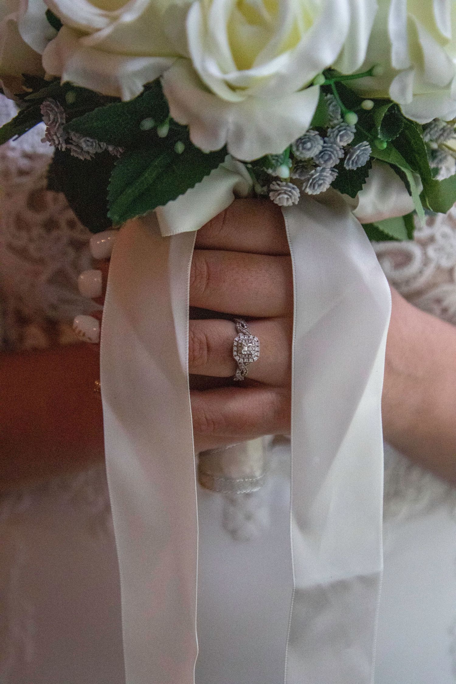 Close-up of an elegant diamond engagement ring with white roses and satin ribbon.